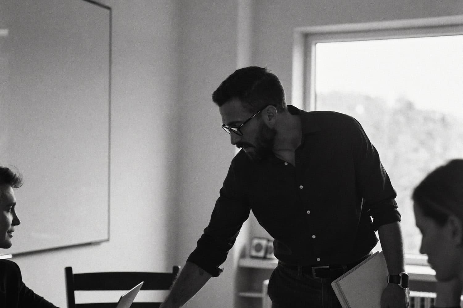 Un homme penché sur la table d'une salle de réunion consulte un document à côté d'un ordinateur portable ouvert